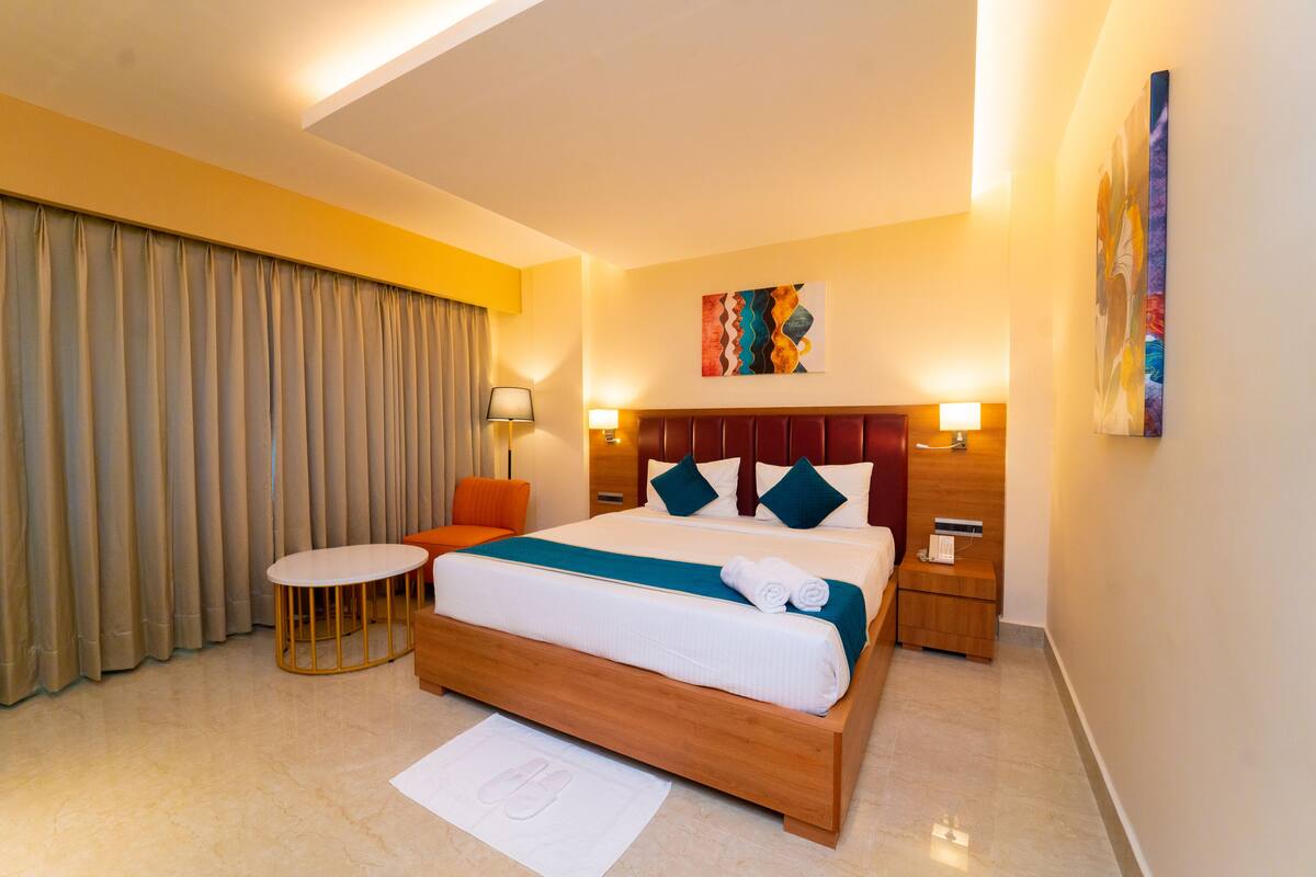 Une chambre d’hôtel avec un grand lit, une table ronde, une chaise et un bureau avec une lampe.