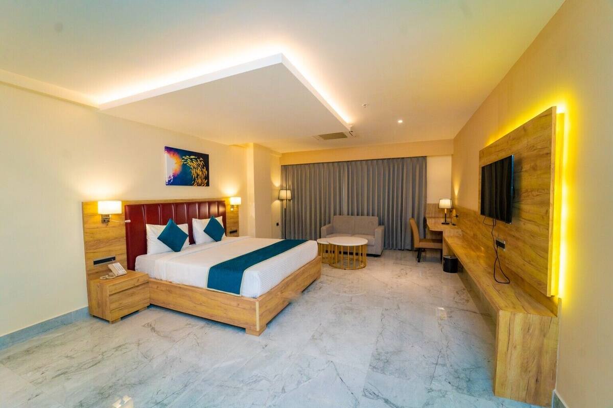 Une chambre d’hôtel avec un grand lit, des tables de chevet, un bureau, une chaise, une télévision et une fenêtre avec des rideaux.