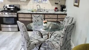 Een moderne keuken met donkere houten kastjes, een roestvrijstalen fornuis en een glazen eettafel omringd door stoelen met een bladmotief.