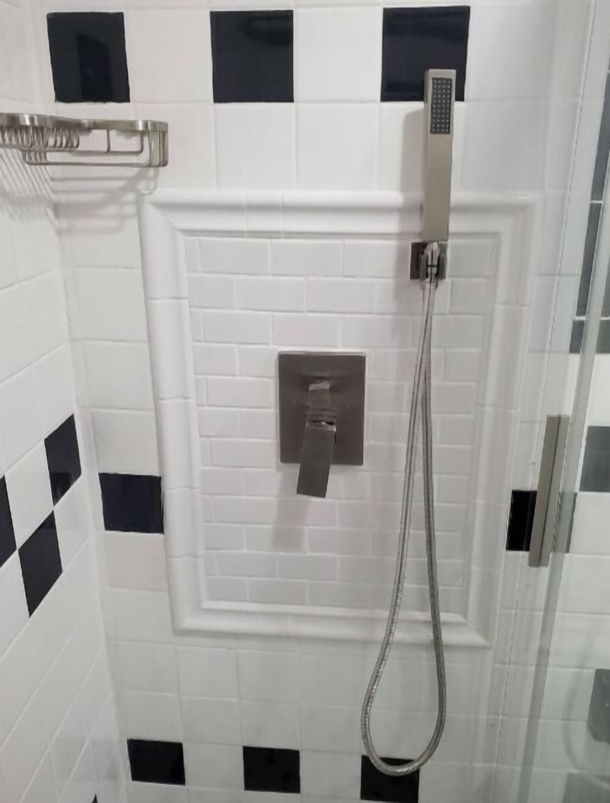 Un área de ducha con cabezal de ducha de mano y panel de control en la pared.