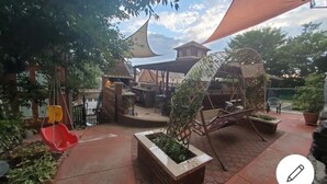 Een terras met een schommel, een plantenbak met planten en een beschaduwd zitgedeelte.