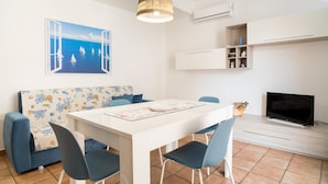 A modern living room with a dining table, chairs, a sofa, a television, and a painting of sailboats. - Apartment 'La Casa Di Terry' with Balcony and Air Conditioning (Acireale)