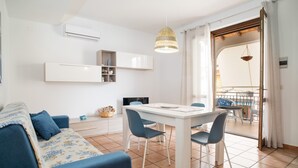 A modern living room with a sofa, dining table, chairs, and a hanging light fixture. - Apartment 'La Casa Di Terry' with Balcony and Air Conditioning (Acireale)