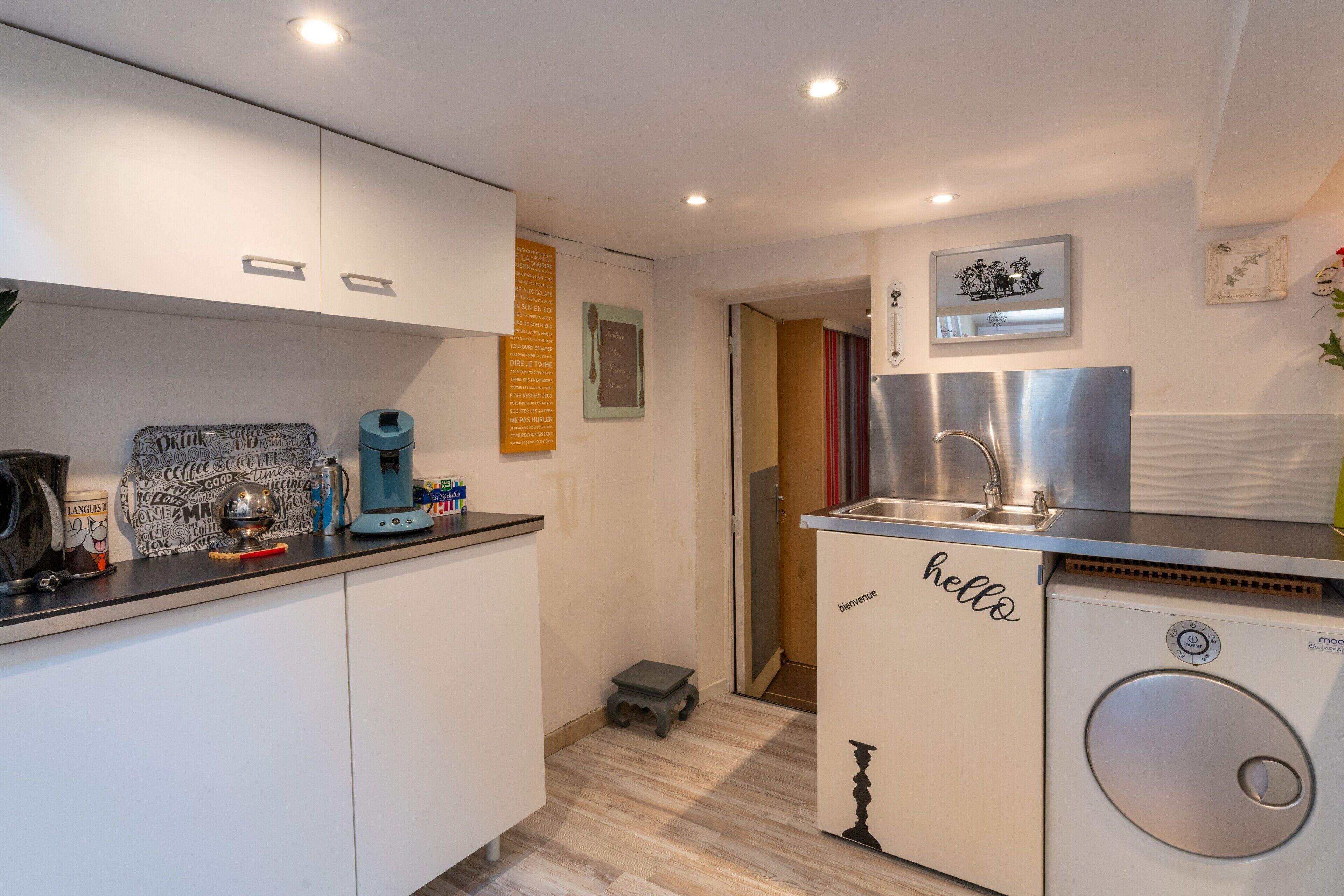 A compact kitchen with white cabinets, a coffee machine, a sink, and a compact washer-dryer unit.