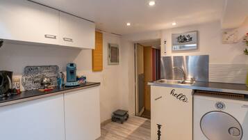 A compact kitchen with white cabinets, a coffee machine, a sink, and a compact washer-dryer unit.