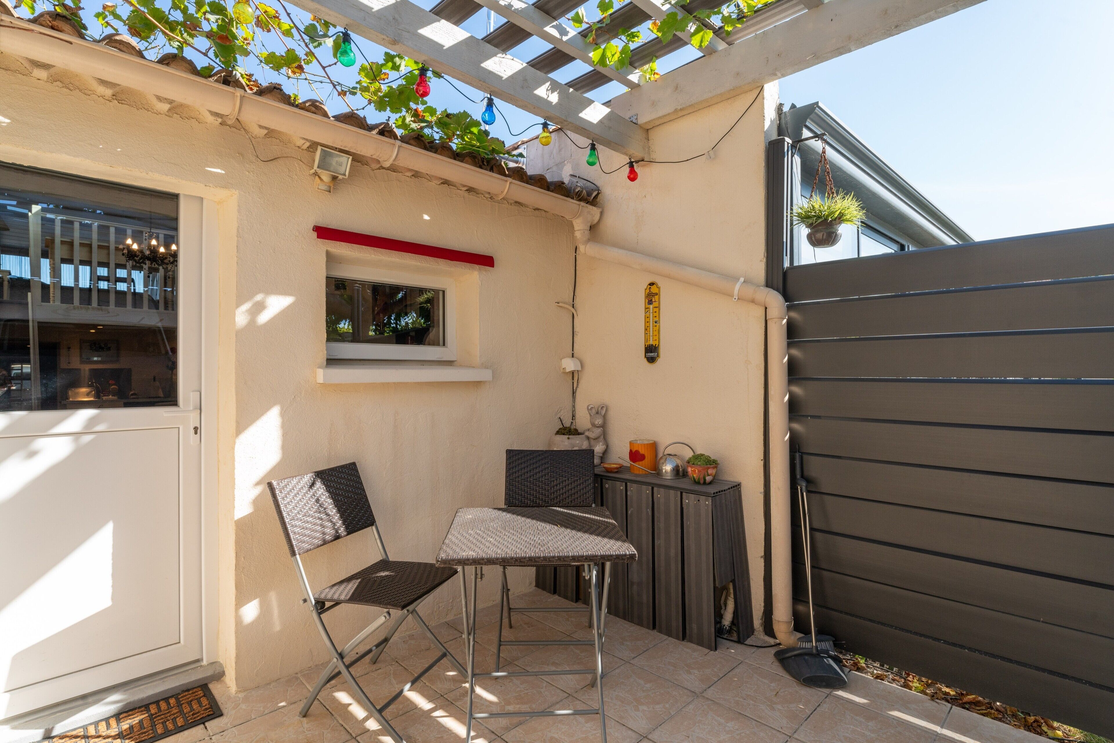 Une terrasse dotée d’une pergola, d’une chaise pliante, d’une petite table et d’une plante en pot.
