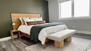 Un dormitorio moderno con cabecera de madera, un ventanal grande y una alfombra estampada.