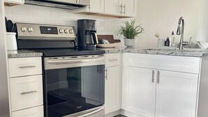 Una cocina moderna con armarios blancos, estufa de acero inoxidable, microondas, cafetera y lavavajillas.