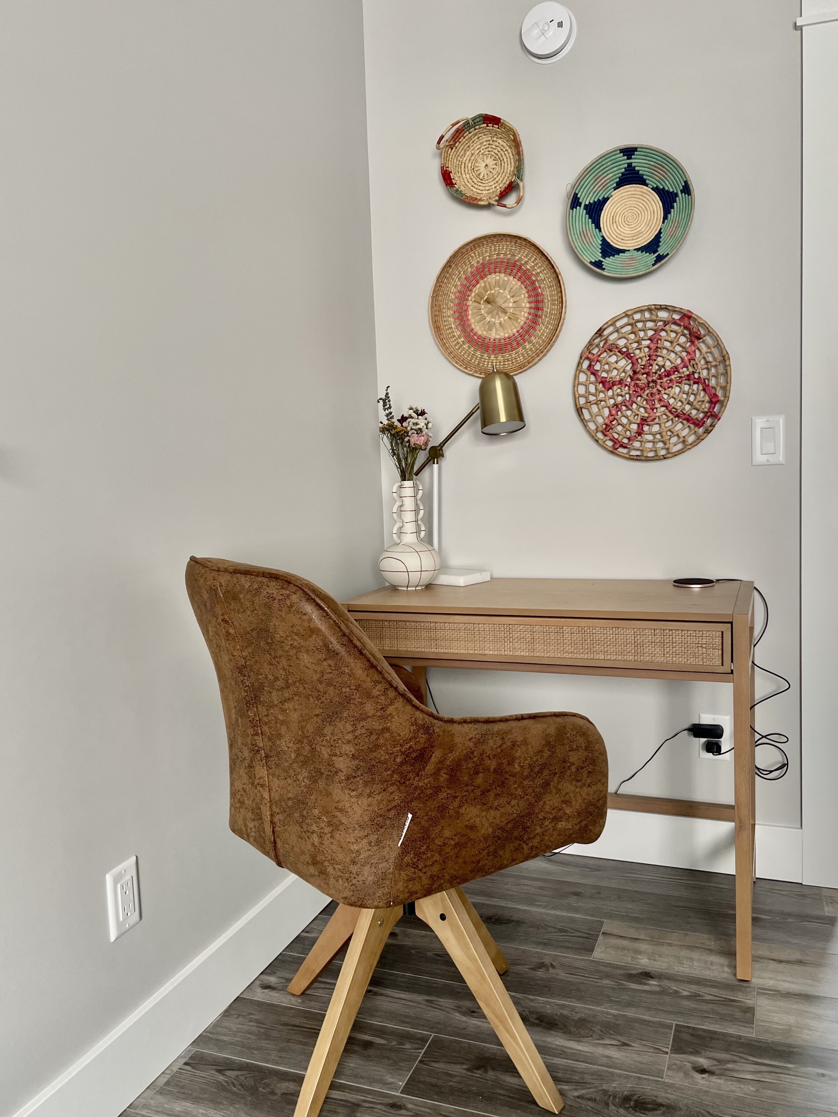 Een moderne kantoorruimte met een houten bureau, een bruine fauteuil en decoratieve geweven borden aan de muur.
