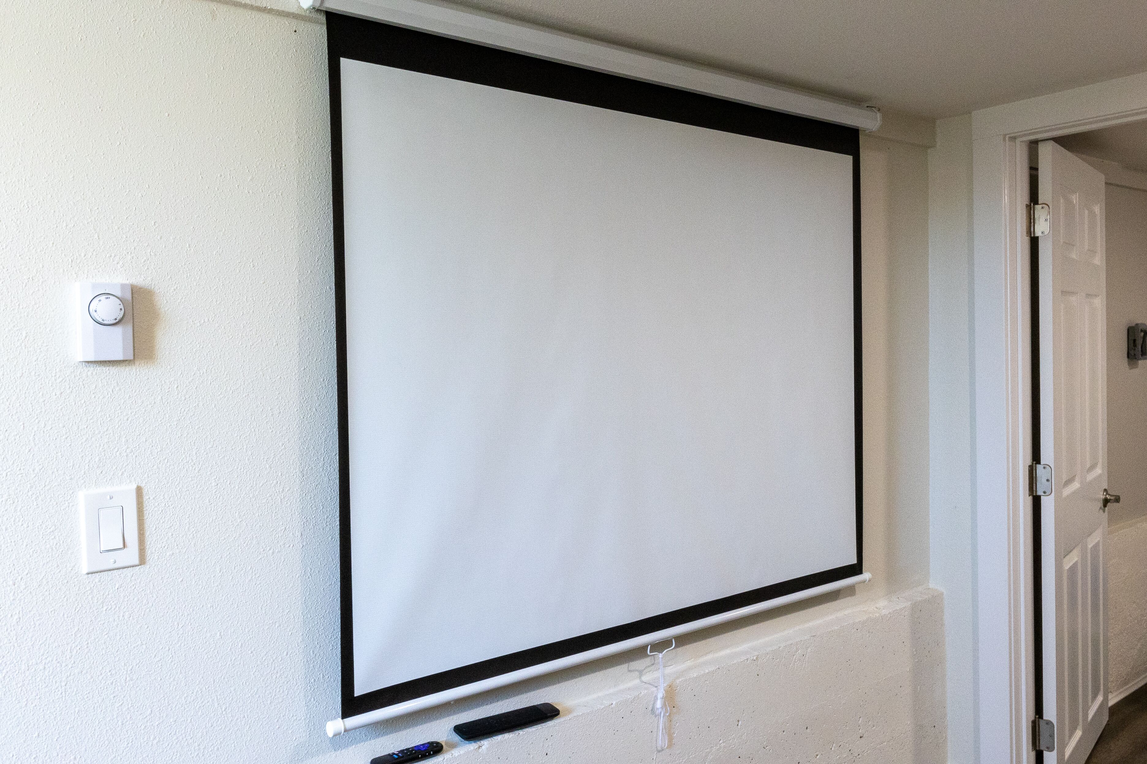 Une pièce dotée d’un grand écran de projection blanc fixé au mur, d’une porte et d’un interrupteur.