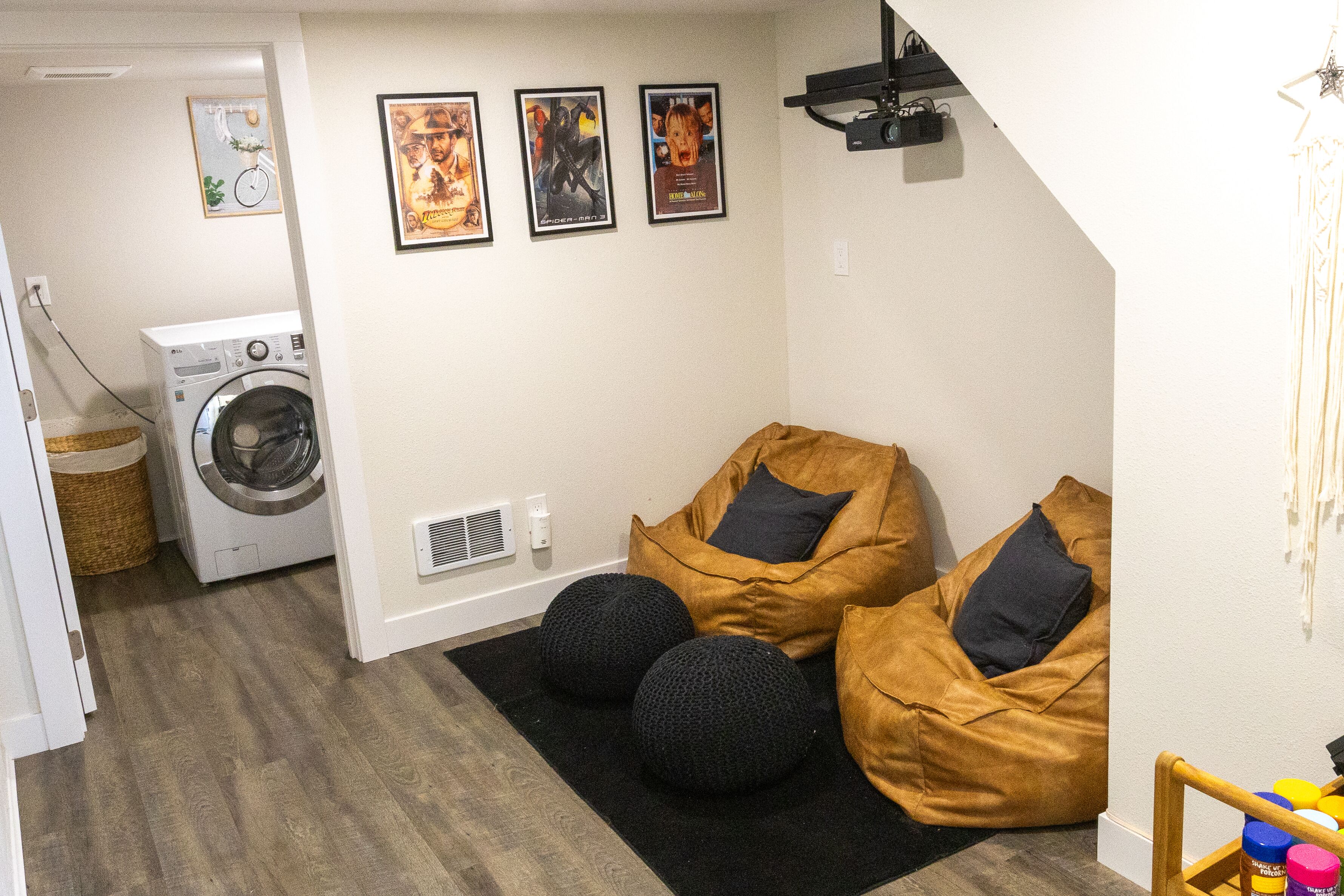 A laundry area with a washing machine, a dryer, and a basket. There are two bean bags with black cushions and a black rug on the floor.