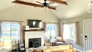 A spacious living room with a fireplace, a large sofa, a television, and a ceiling fan. - Waddle on Inn-Ocean Park Cottage (Ocean Park)