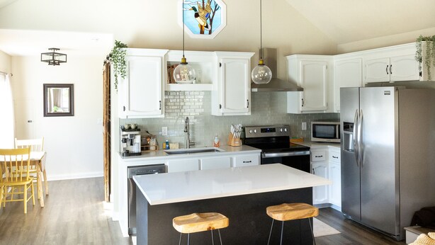 A modern kitchen with white cabinets, stainless steel appliances, and a central island with bar stools. - Waddle on Inn-Ocean Park Cottage (Ocean Park)