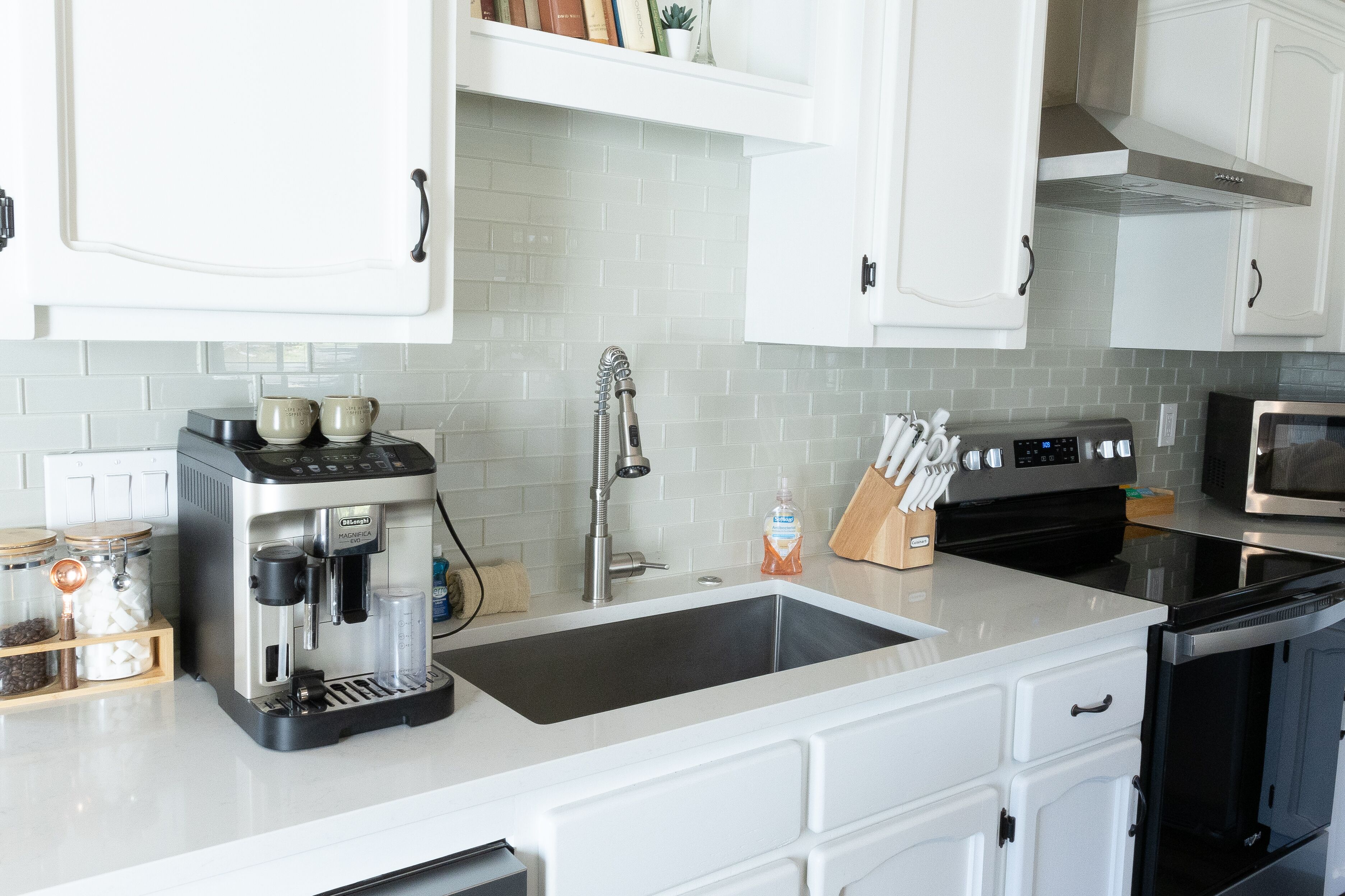 A modern kitchen with white cabinets, a stainless steel espresso machine, a sink, and a microwave.