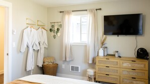 A bedroom with a bed, a TV mounted on the wall, a dresser, and a window with curtains. - Waddle on Inn-Ocean Park Cottage (Ocean Park)