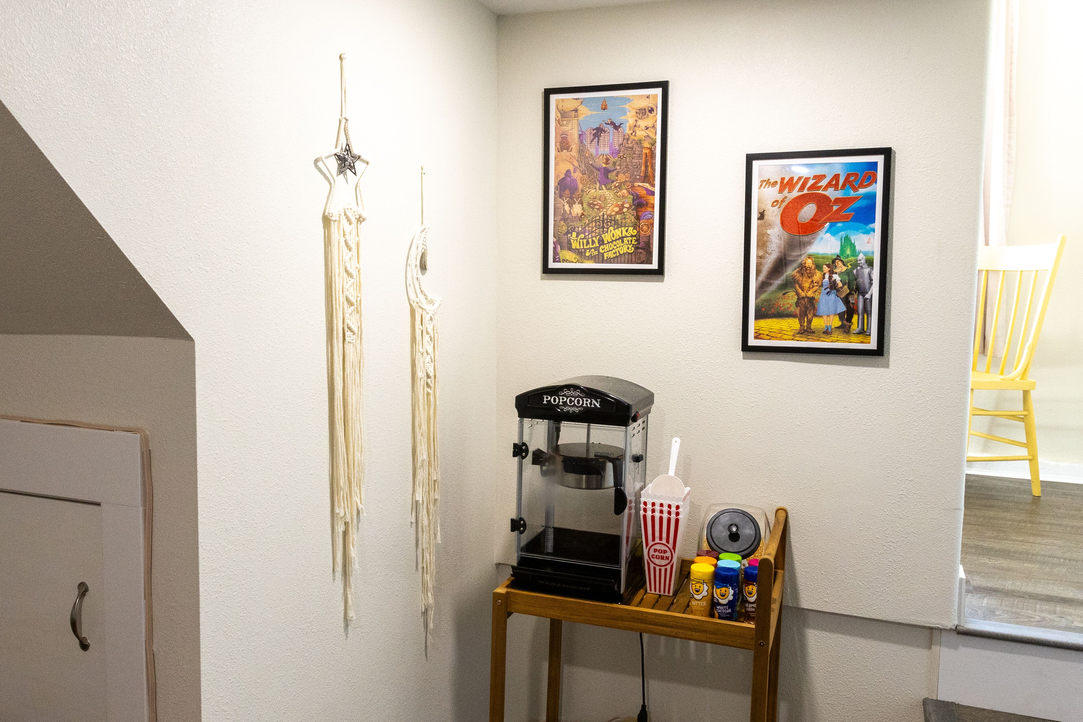 Une pièce équipée d’un appareil à pop-corn, de deux affiches encadrées, d’une petite table avec des collations et d’une chaise.