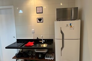 A compact kitchen with a refrigerator, microwave, sink, and a small countertop.