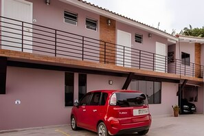 Een rode auto geparkeerd voor een gebouw met twee verdiepingen, een balkon en een garage.