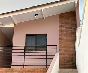Un edificio moderno con balcón, una ventana con cortinas y una pared de ladrillo.