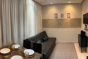 Un salon moderne avec un canapé, une table à manger dressée avec des assiettes et des verres, un tapis à motifs et un téléviseur fixé au mur.
