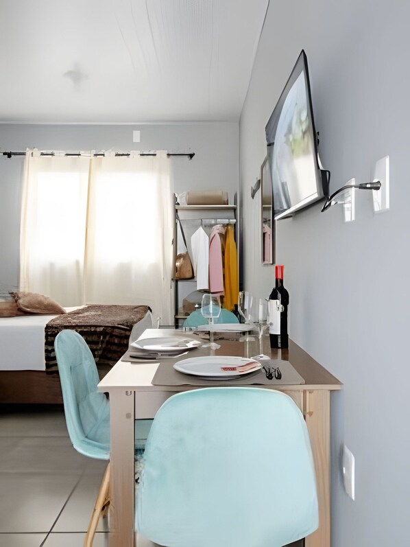 Une chambre d’hôtel comprenant un lit, un bureau avec une chaise, un téléviseur fixé au mur et une fenêtre avec des rideaux.