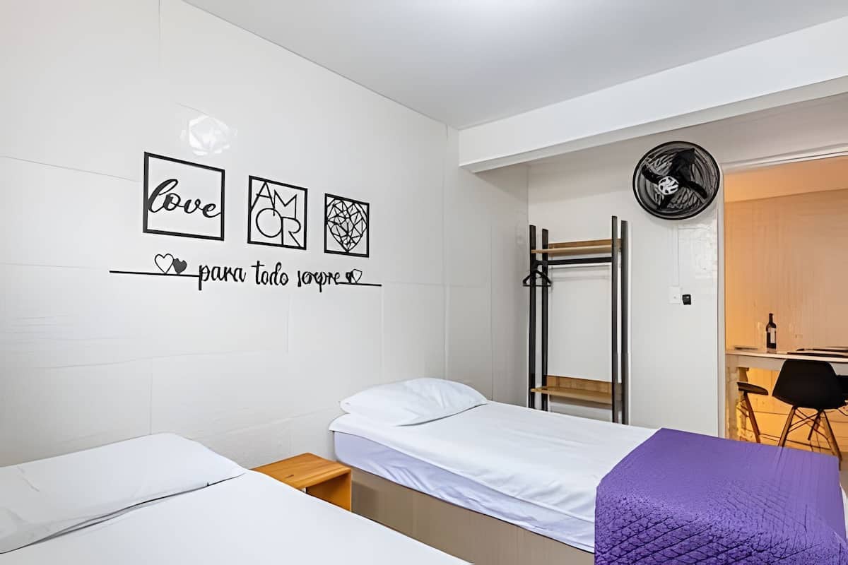 A bedroom with two beds, a wall with decorative art, a fan, and a desk with a chair.