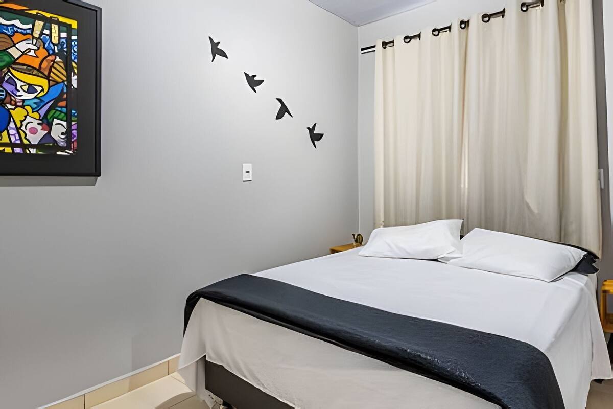 Une chambre à coucher avec un lit, un interrupteur fixé au mur et une œuvre d’art aux couleurs vives.