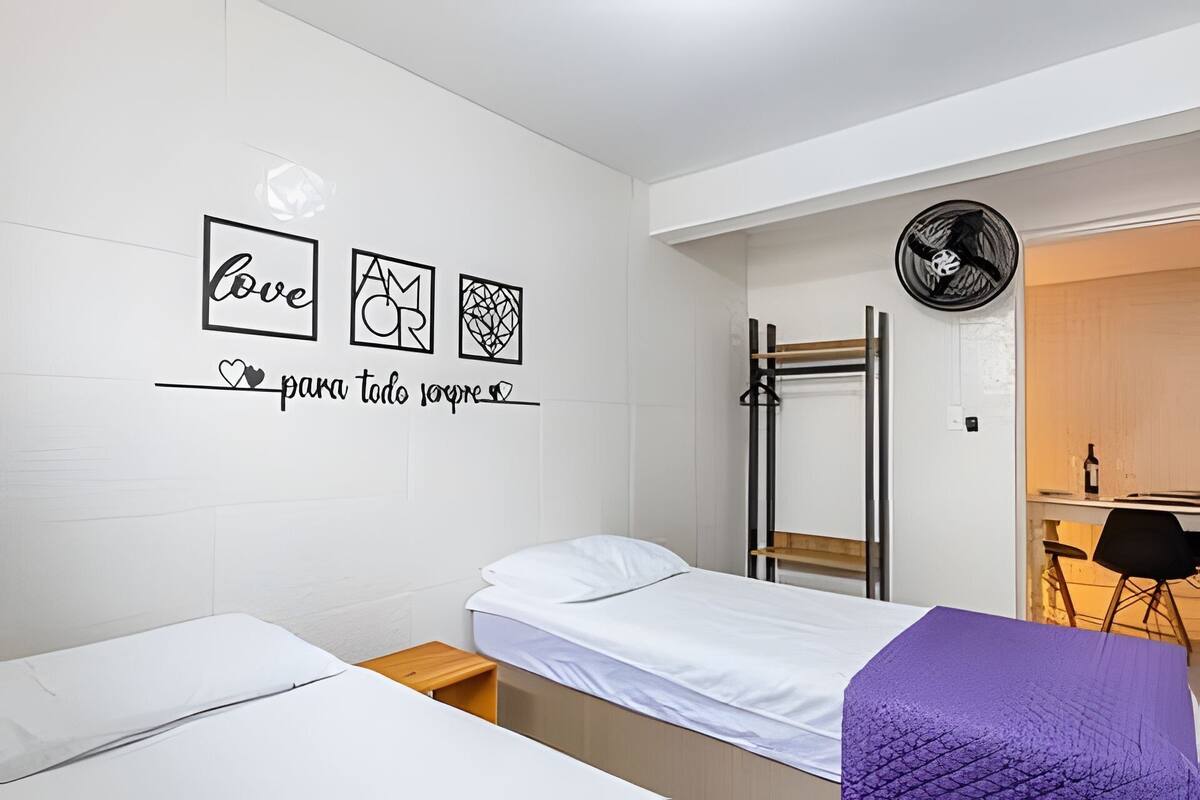 Une chambre avec deux lits, un mur décoré d’œuvres d’art, un ventilateur et un bureau avec une chaise.