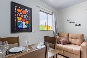 Een woonkamer met een bank, een eettafel met stoelen, een lijst met abstract schilderij, en een raam met gordijnen.