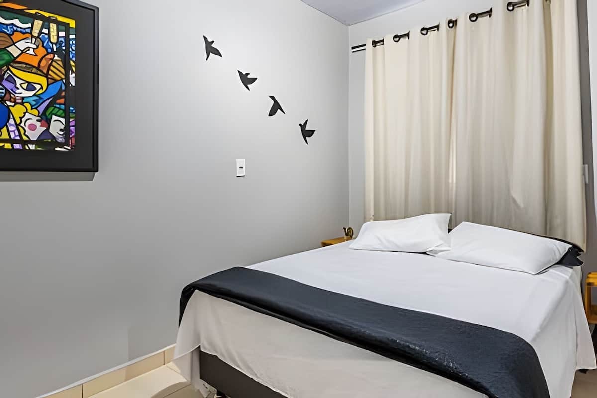 A bedroom with a bed, a wall-mounted light switch, and a colorful artwork.