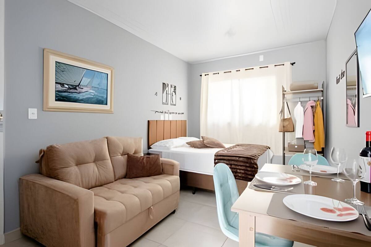 Une chambre d’hôtel comprenant un lit, un canapé, une table à manger avec des assiettes et des verres à vin, un miroir et un porte-manteau avec des vêtements.