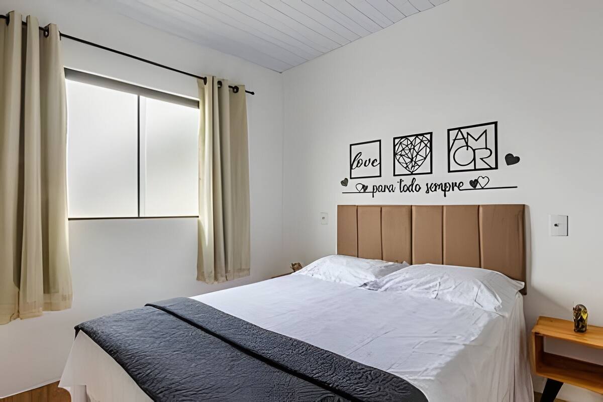 Une chambre à coucher avec un lit, des rideaux, un mur décoré d’œuvres d’art et une table de chevet en bois.