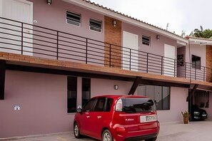 Un coche rojo estacionado frente a un edificio con balcón y garaje.