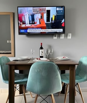 Uma sala de jantar com televisão na parede, uma garrafa de vinho e duas cadeiras.