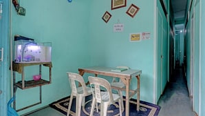 Una habitación con paredes verde azulado, una mesa de madera, dos sillas de plástico, un acuario y un estante con un cuenco rosa.