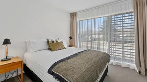 Une chambre à coucher avec un lit, une table de chevet, une lampe et une fenêtre avec des rideaux.