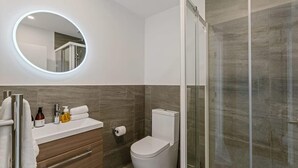Une salle de bain moderne avec un grand miroir rond, des toilettes et un espace douche.