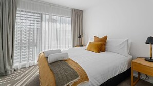 A hotel room with a large bed, a bedside table with a lamp, and sheer curtains on the windows.