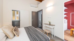 A bedroom with a bed, bedside table, and a desk with a chair. There is a door leading to another room and a radiator on the wall. - NEW! Design & Modern Flat in Trastevere (Roma)