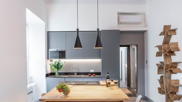 A modern kitchen with dark cabinets, a wooden ceiling, pendant lights, a central island with a vase of flowers, and a wine bottle. - NEW! Design & Modern Flat in Trastevere (Roma)