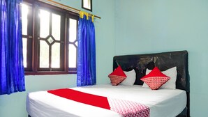 A bed with a white and red bedspread, two red pillows, and a window with blue curtains. - OYO 92997 Villa Hj Karnadi (Cisarua)