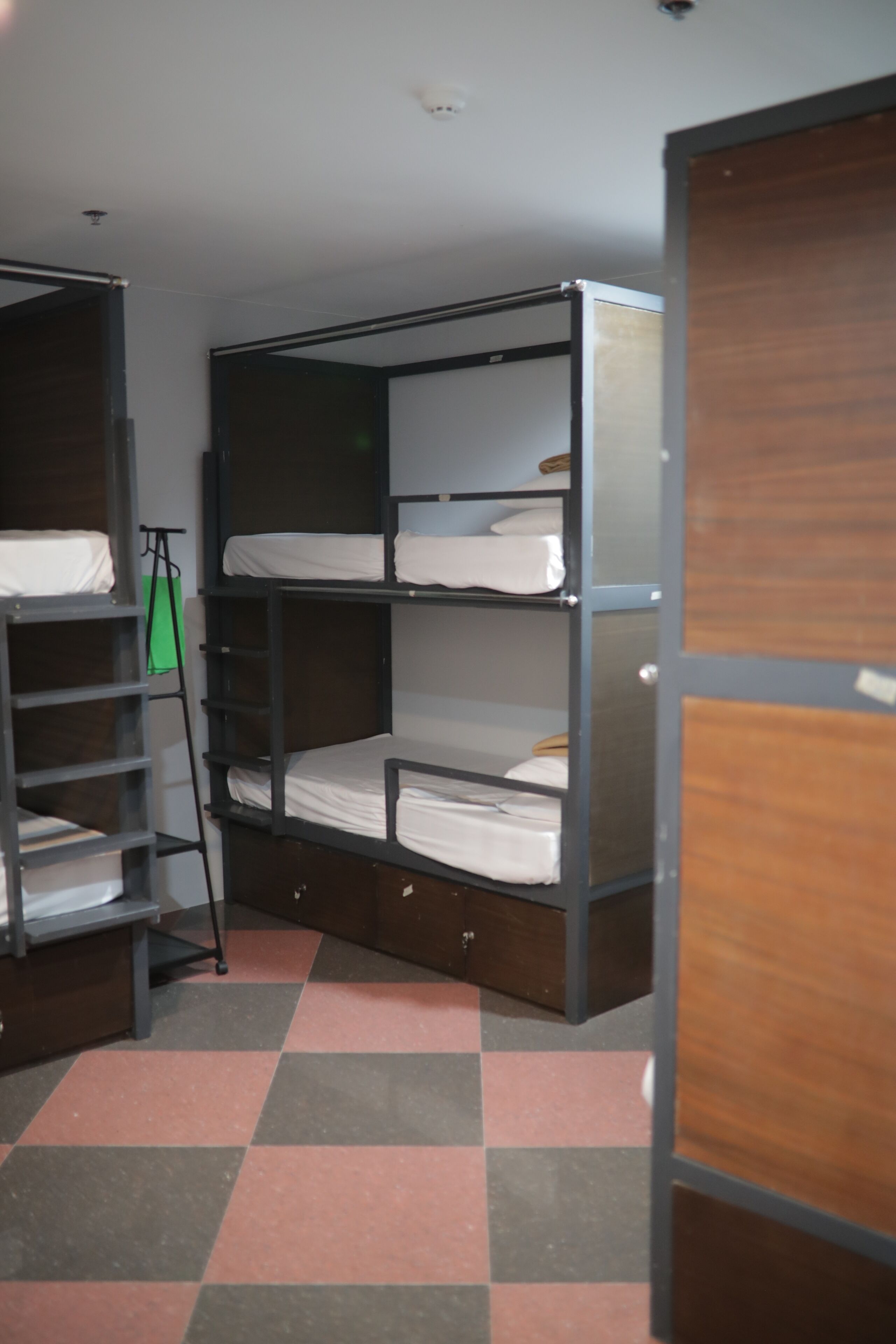 Camera con letto a castello, pavimento a scacchi, scala e una borsa verde appesa al muro.