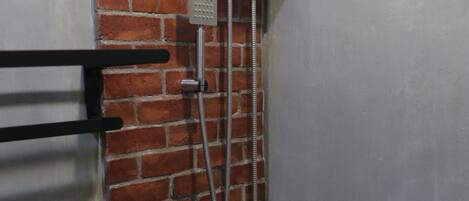 A shower area with a metal hose and a control panel mounted on a brick wall.
