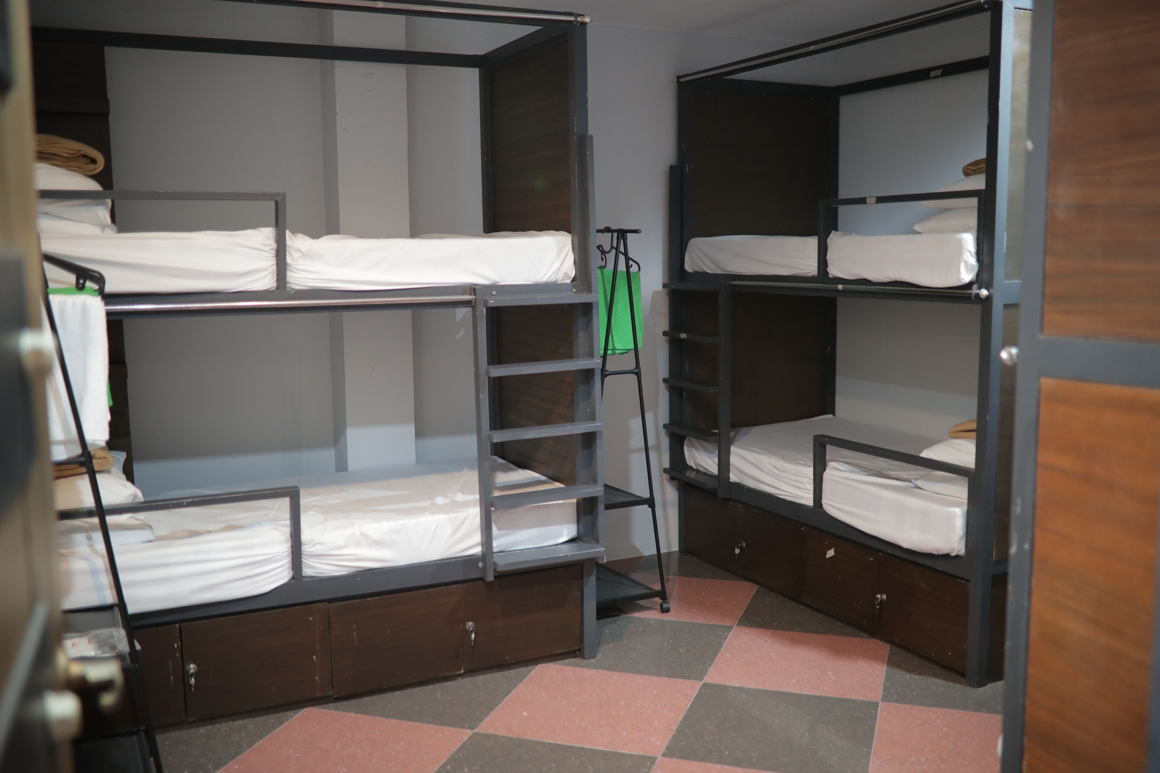 A dormitory room with bunk beds, a green hanging rack, and a checkered floor.