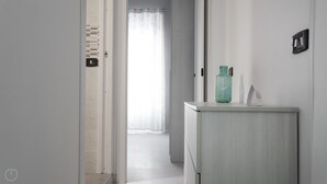 Un corridoio con una porta che conduce al bagno, una parete di colore chiaro e un piccolo mobile con una bottiglia verde sopra.