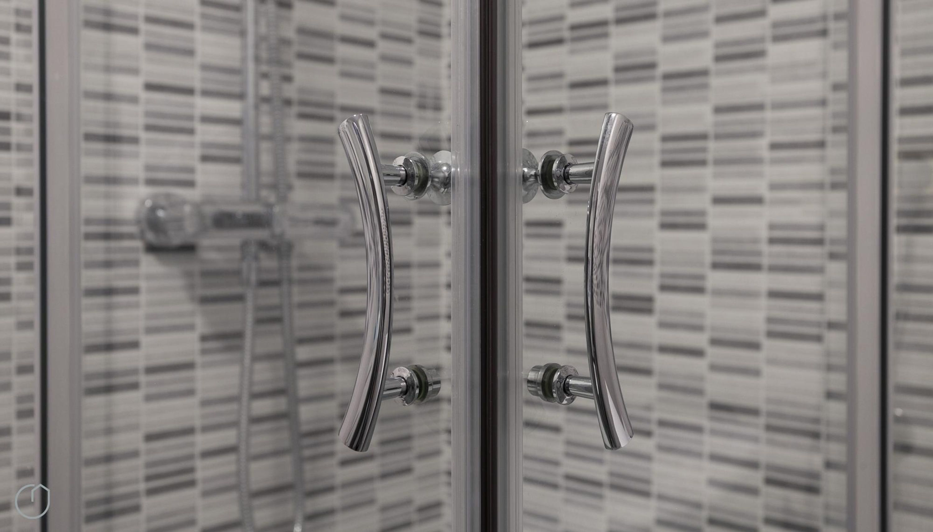A bathroom with a glass shower door and a tiled wall.