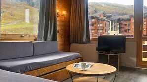 Moderni hotellihuone, jossa on puuseinä, sohva, televisio ja näkymä hiihtokeskukseen.