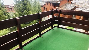 Un balcón con alfombra verde, baranda de madera y vista de edificios y árboles circundantes.