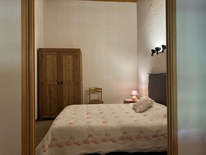 A bedroom with a bed, a wooden wardrobe, a chair, a bedside table with a lamp, and a wall-mounted light fixture. - Teppes 46 - Cosy duplex ski in, ski out (LES AVANCHERS VALMOREL)
