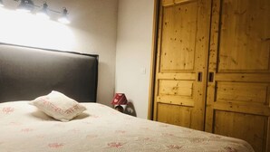 Un dormitorio con una cama, un armario de madera, una lámpara de noche y un aplique de pared.